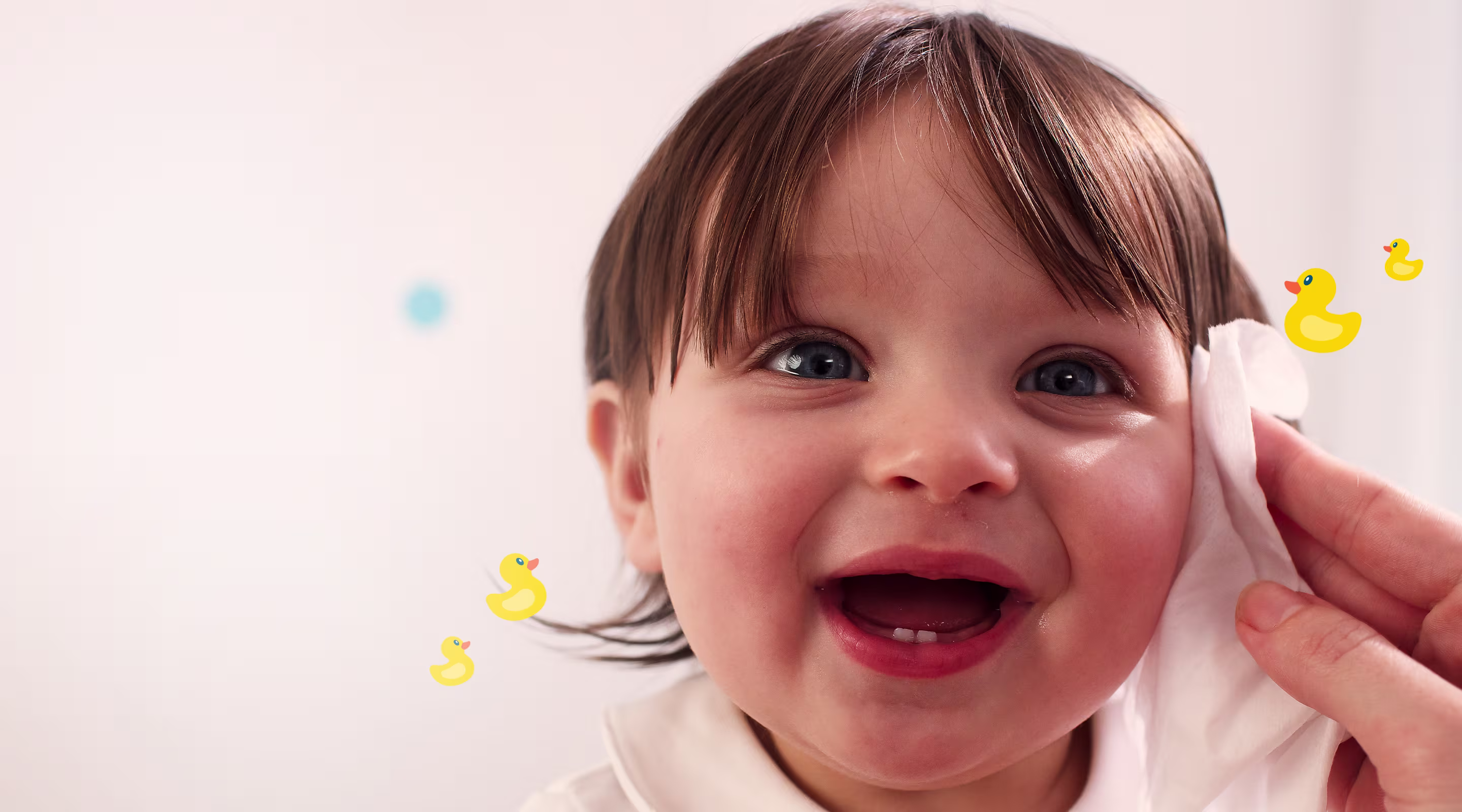 Een close-up van het gezicht van een baby, terwijl een hand zachtjes de wang schoonmaakt met een Pampers Fresh & Clean doekje.