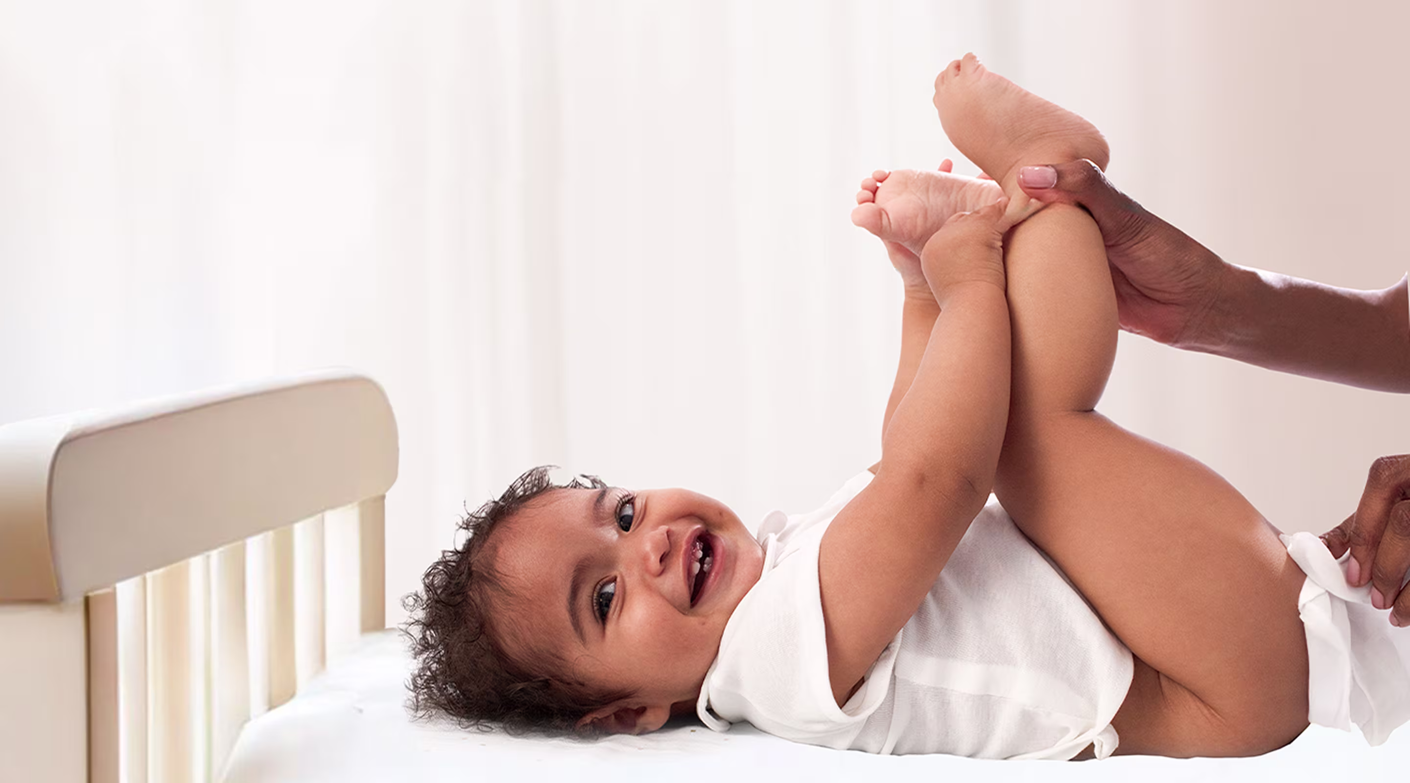 Un bebé está tumbado de espaldas sobre una superficie blanca, sosteniendo sus pies hacia arriba mientras un padre utiliza una toallita para limpiar el trasero del bebé.