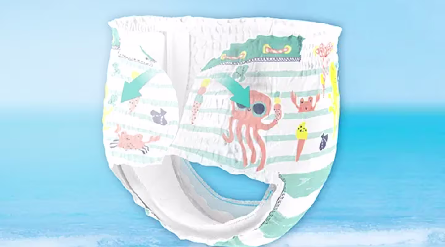 Un primer plano circular muestra unas flechas que abren el lateral de un pañal de baño con temática de Baby Shark en el culito de un bebé.