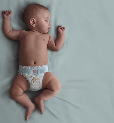 Niemowlę w pieluszce Pampers śpi na plecach na turkusowym kocyku Niemowlę w pieluszce Pampers śpi na plecach na turkusowym kocyku