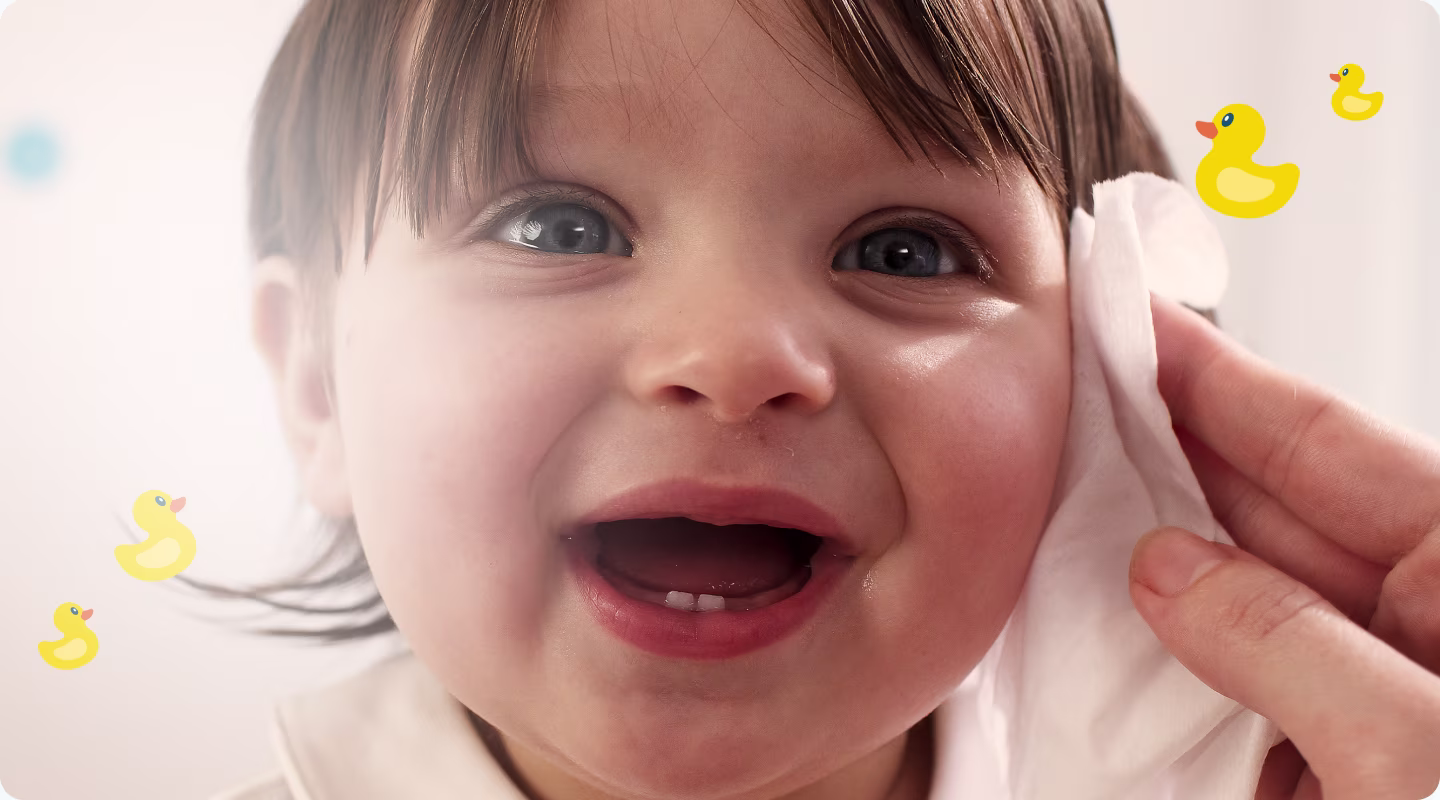 A close-up of a baby's face as a hand gently wipes their cheek with a Pampers Fresh Clean baby wipe.