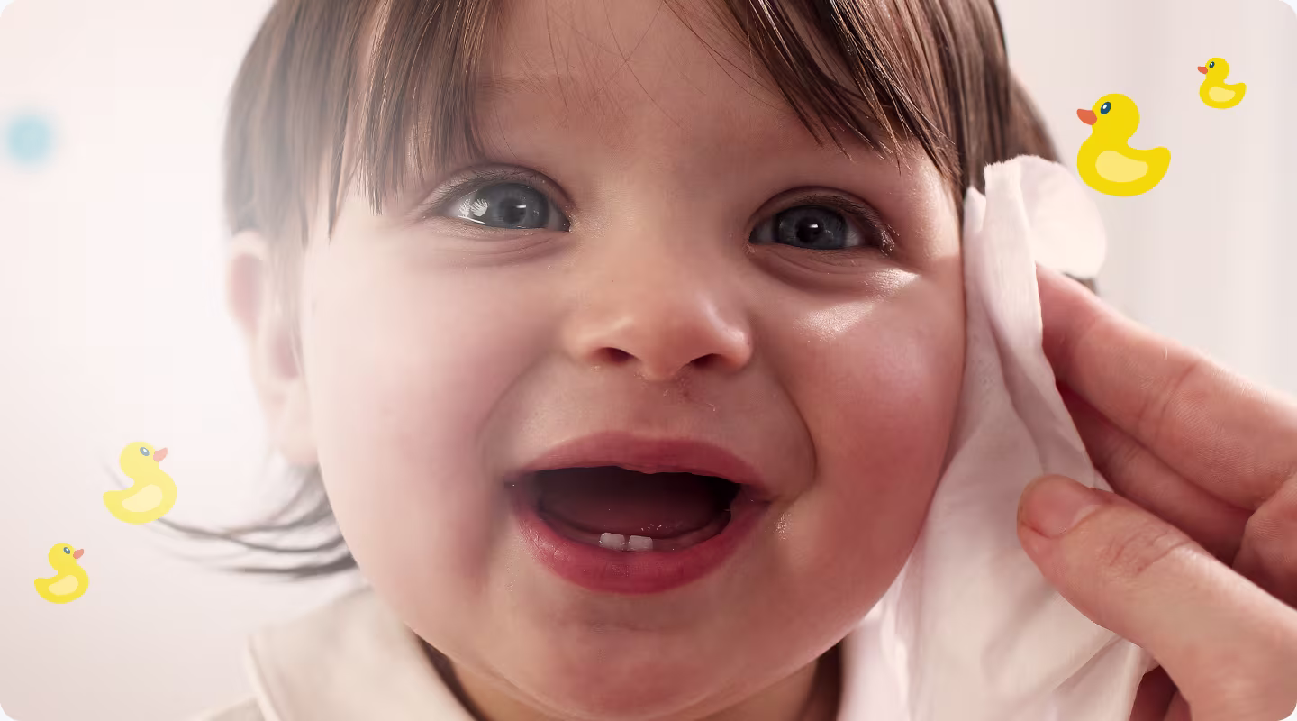 A close-up of a baby's face as a hand gently wipes their cheek with a Pampers Fresh Clean baby wipe.