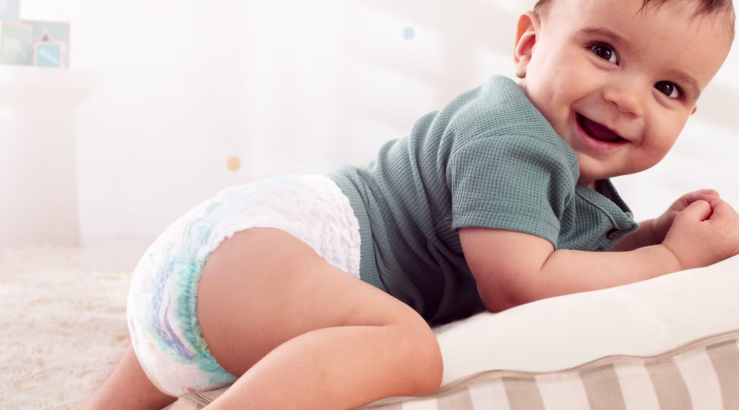 Um bebé que usa uma fralda-cueca Dodot rasteja sobre um suave tapete azul.