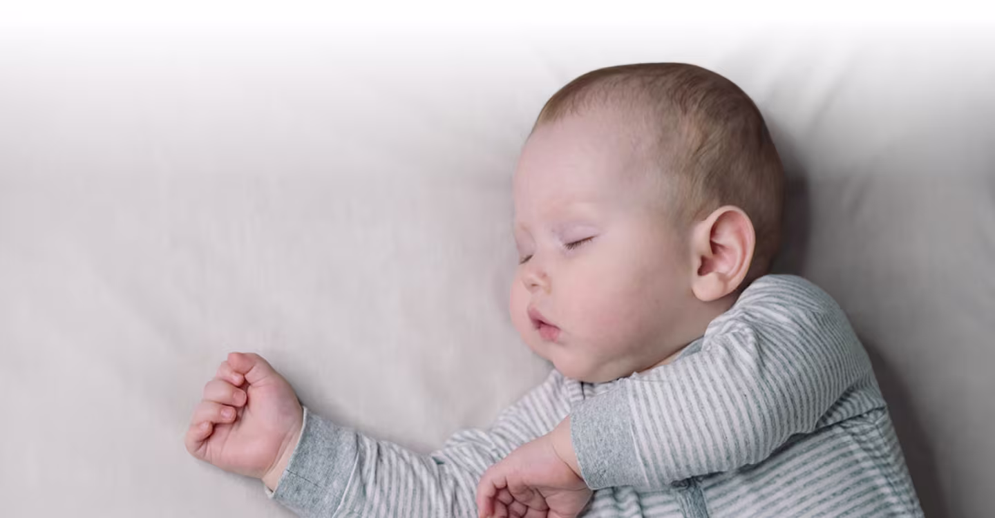 A baby is sleeping peacefully in a bassinet, swaddled in a soft white blanket.