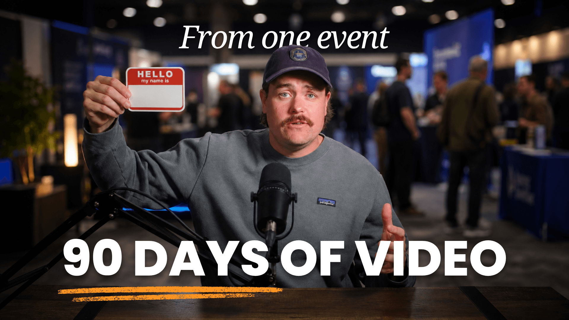 Producer Dave at a desk microphone holding up a blank name tag in front of a busy conference floor.