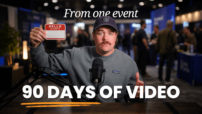 Producer Dave at a desk microphone holding up a blank name tag in front of a busy conference floor.