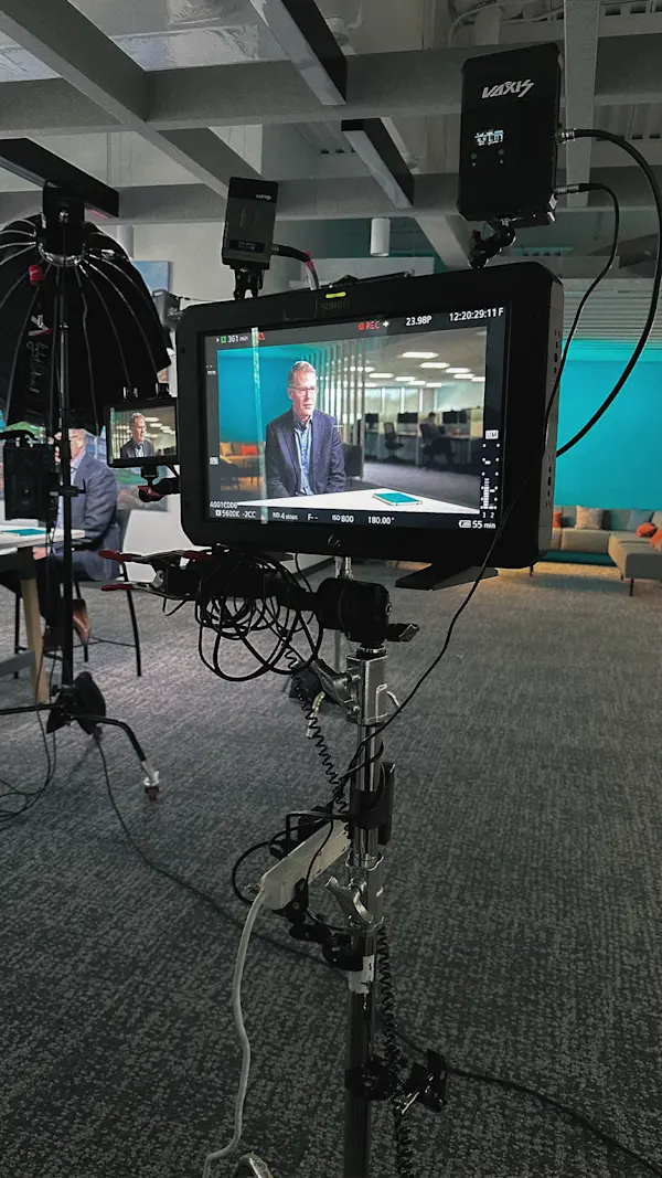 A field monitor shows the framed interview shot while the real interview runs in the background.