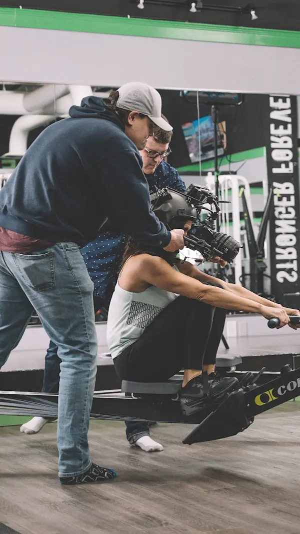 Grip supporting the POV helmet camera rig as an actor rows on a rowing machine.