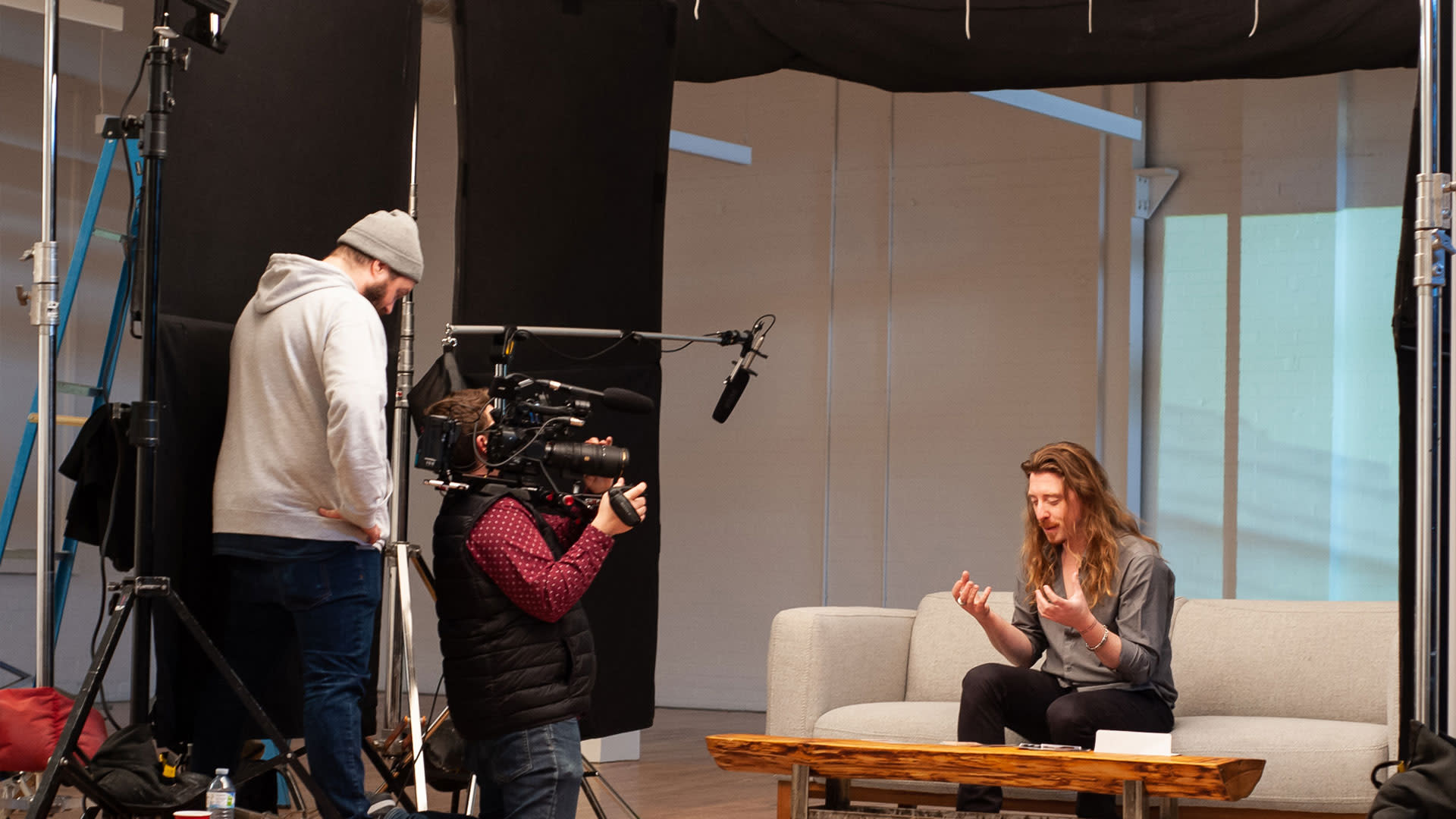 An executive seated on a couch in front of a videographer and lights during a corporate interview video shoot