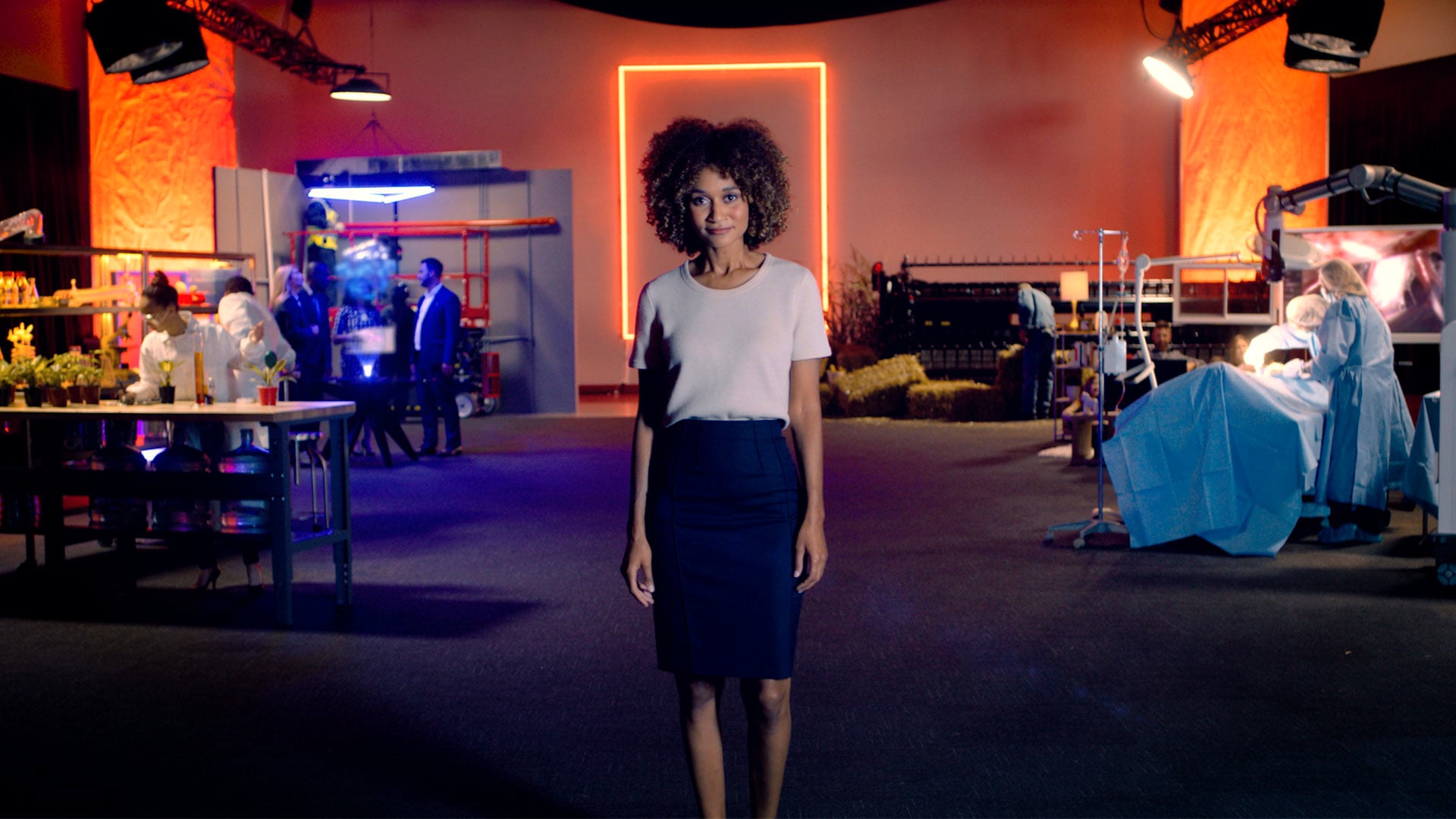 A host stands in a studio surrounded by lab, industrial, farm, and surgical sets in a still from Linamar's brand film.