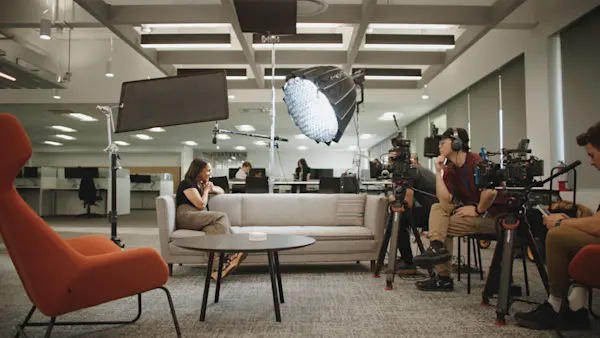 Wide shot of a sofa interview in an open office, with three cameras, a large softbox and crew.