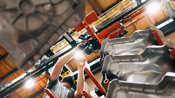 Crew member rigging a camera to overhead equipment beside metal parts in 2CM Innovative's facility