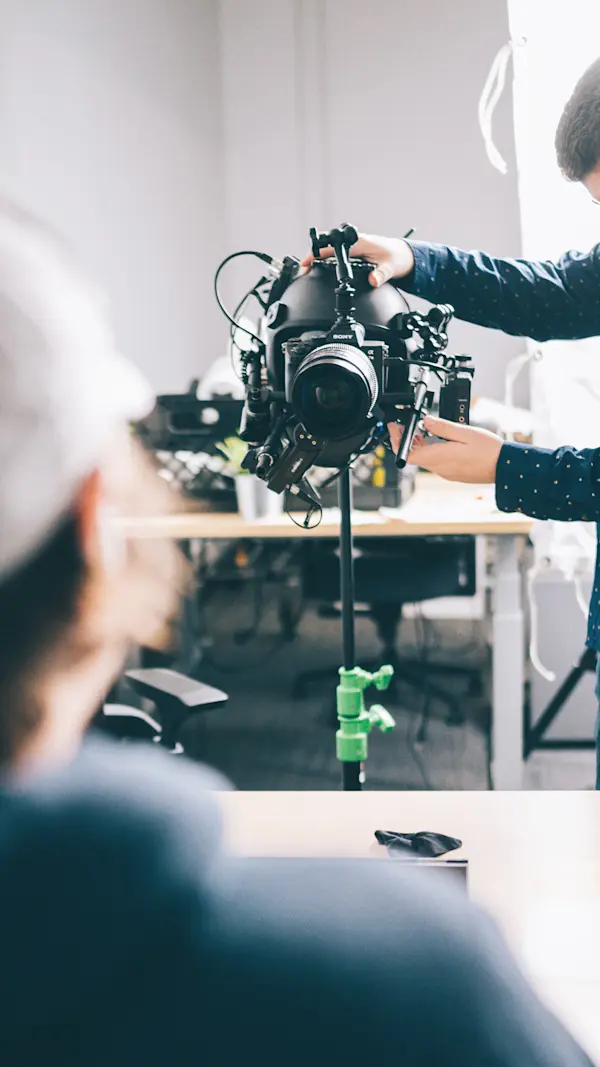 Crew member adjusting a camera mounted on a POV helmet rig, set on a stand in an office.