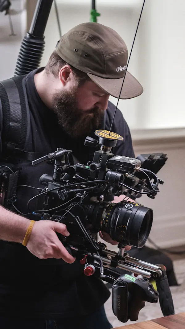 Camera operator adjusting a cinema camera with a large prime lens, mounted on a body-worn support rig