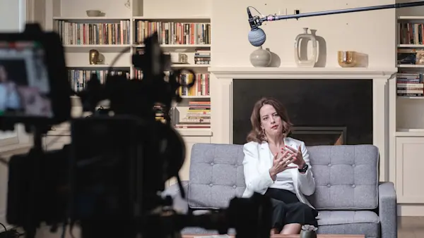 Financial advisor speaking on a couch by the fireplace, with a cinema camera out of focus in the foreground