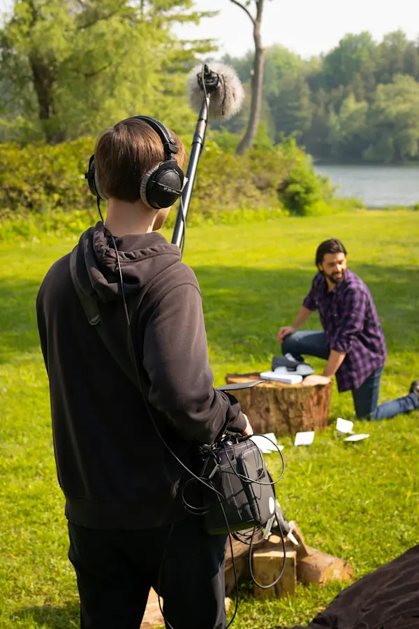 Boom operator recording an actor kneeling by a tree stump on the lakeside Fairstone set
