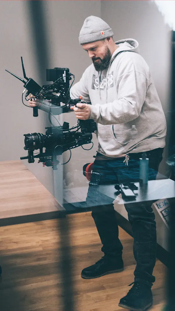 Crew member in a grey hoodie and toque holding a camera gimbal in an office.
