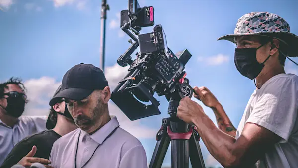 A camera operator in a bucket hat frames the coach as he looks down at a pair of white sneakers.