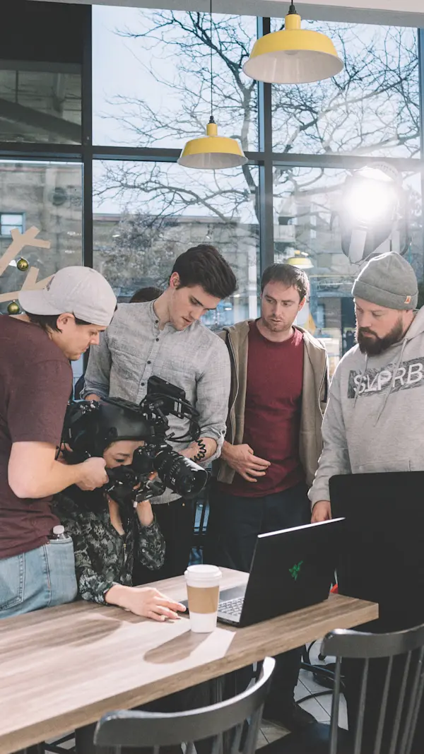 Film crew gathered around an actor in the helmet rig at a table with a laptop and a coffee.