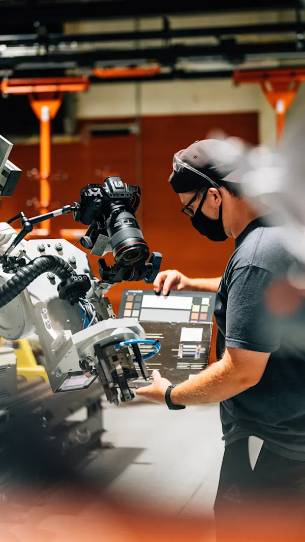 Crew member holding a colour chart in front of an industrial robot fitted with a camera at 2CM Innovative