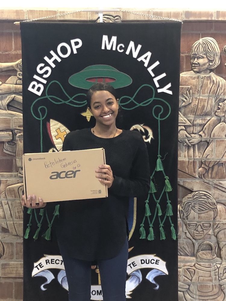 A happy student in front of a Bishop McNally banner holds a cardboard box labeled 'Acer'