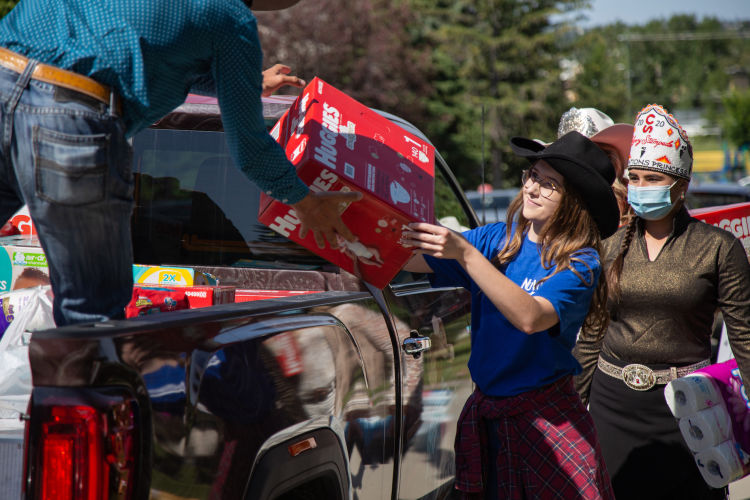A woman in a black cowboy hat delivers a red box of Huggies Diapers to another volunteer