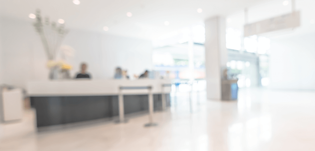 Blurred view of a modern reception area with white walls, dark counter, and bright lighting in a corporate lobby.