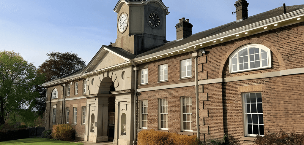 Historic brick building with clock tower, arched entrance, and multiple windows against a blue sky.