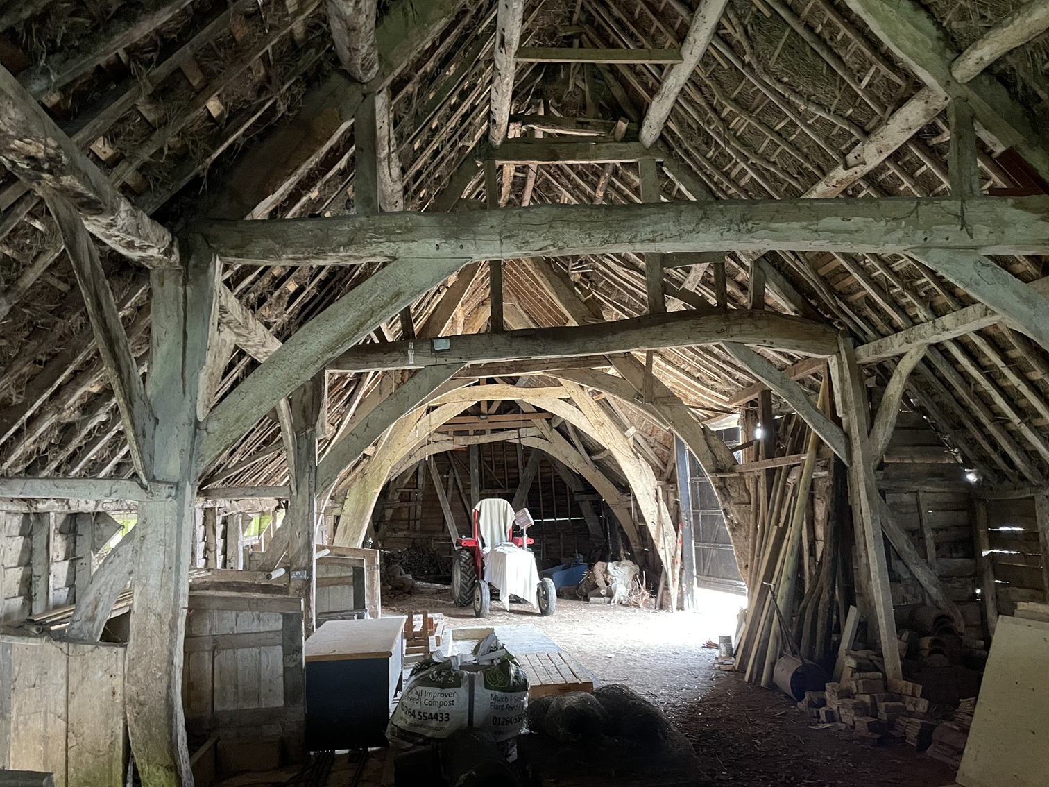 Interior of rustic wooden barn with exposed timber frame structure and a small red tractor visible in the background.