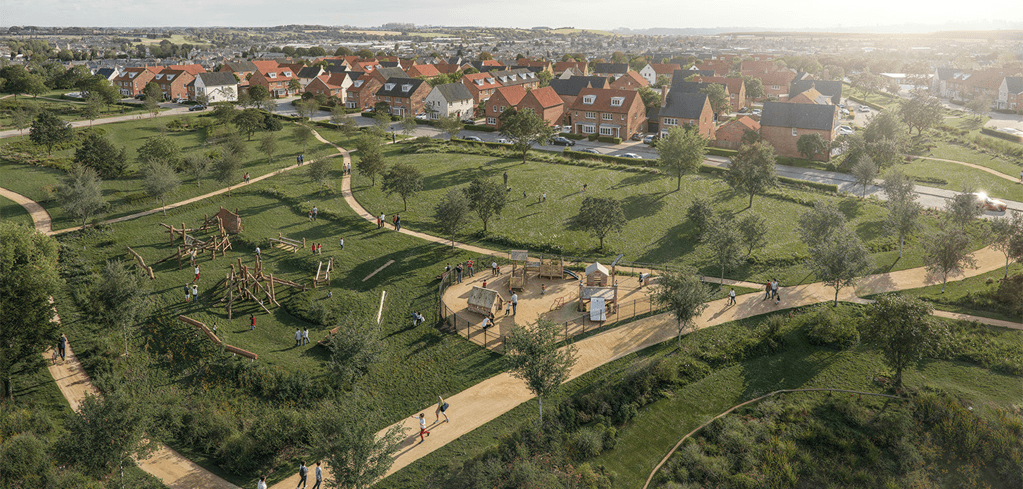Aerial view of a green park with play areas, winding paths, trees, and a residential neighborhood with red-brick houses in the background.