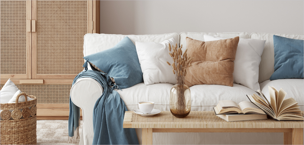 Cozy white sofa with blue and brown pillows, wooden coffee table with open book and dried flowers in modern living room.