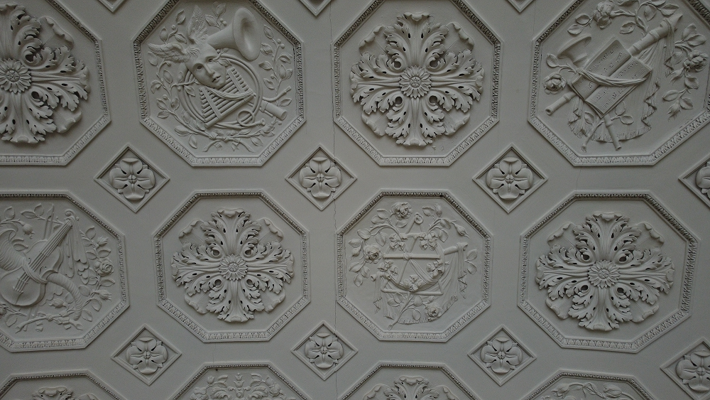 Ornate white ceiling with octagonal panels featuring detailed relief carvings of musical instruments and floral designs.