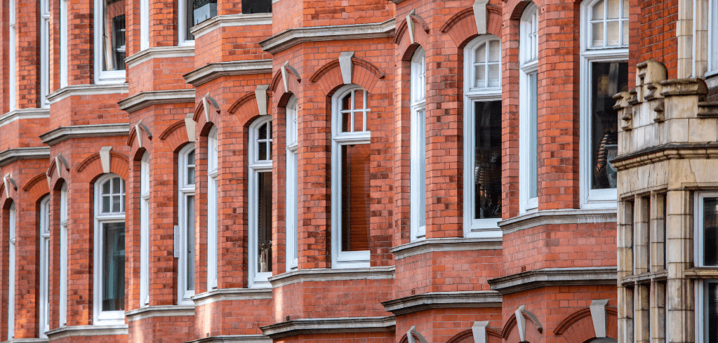 Row of traditional red brick Victorian townhouses with white-framed windows and decorative arched architectural details.