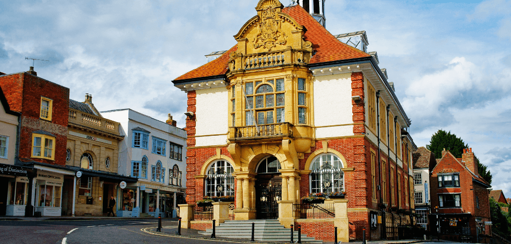 Historic brick and stone town hall with ornate golden facade and red roof, situated on a quiet street corner.