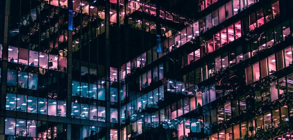 Modern office building at night with illuminated windows glowing pink and blue, creating a vibrant urban landscape.
