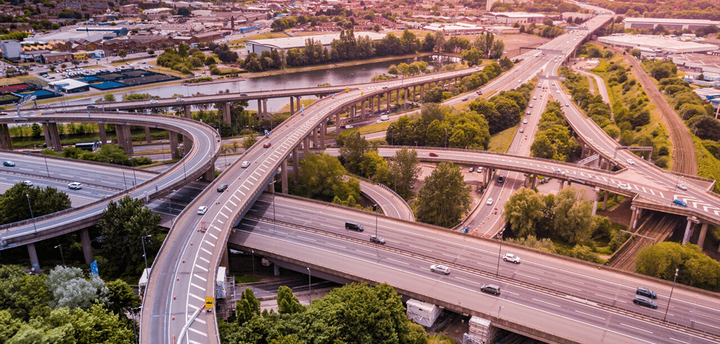Aerial view of complex highway interchange with multiple elevated roads, bridges crossing a river, and surrounding greenery.