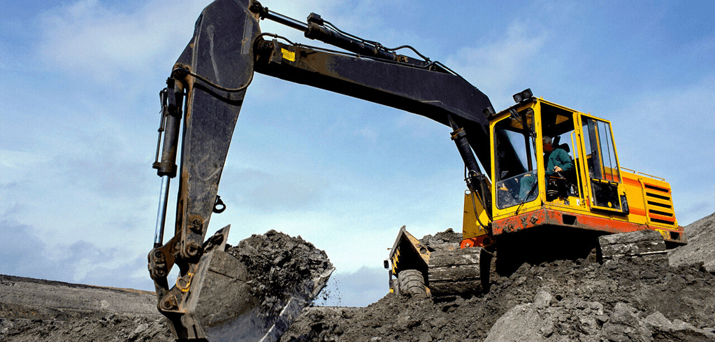 Yellow and black excavator with extended arm digging into soil at a construction site under blue sky.