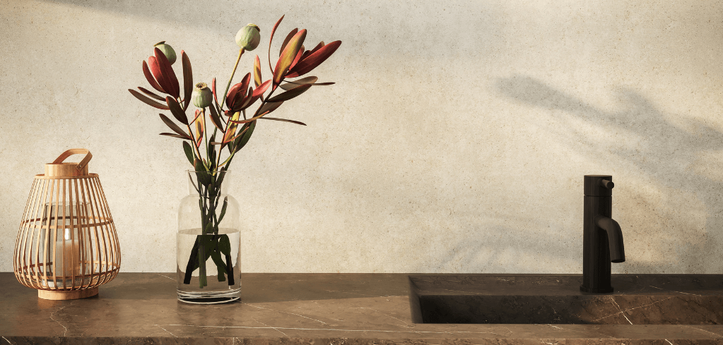 A marble countertop with a bamboo lantern, glass vase of red flowers, and a dark matte faucet over a sink.