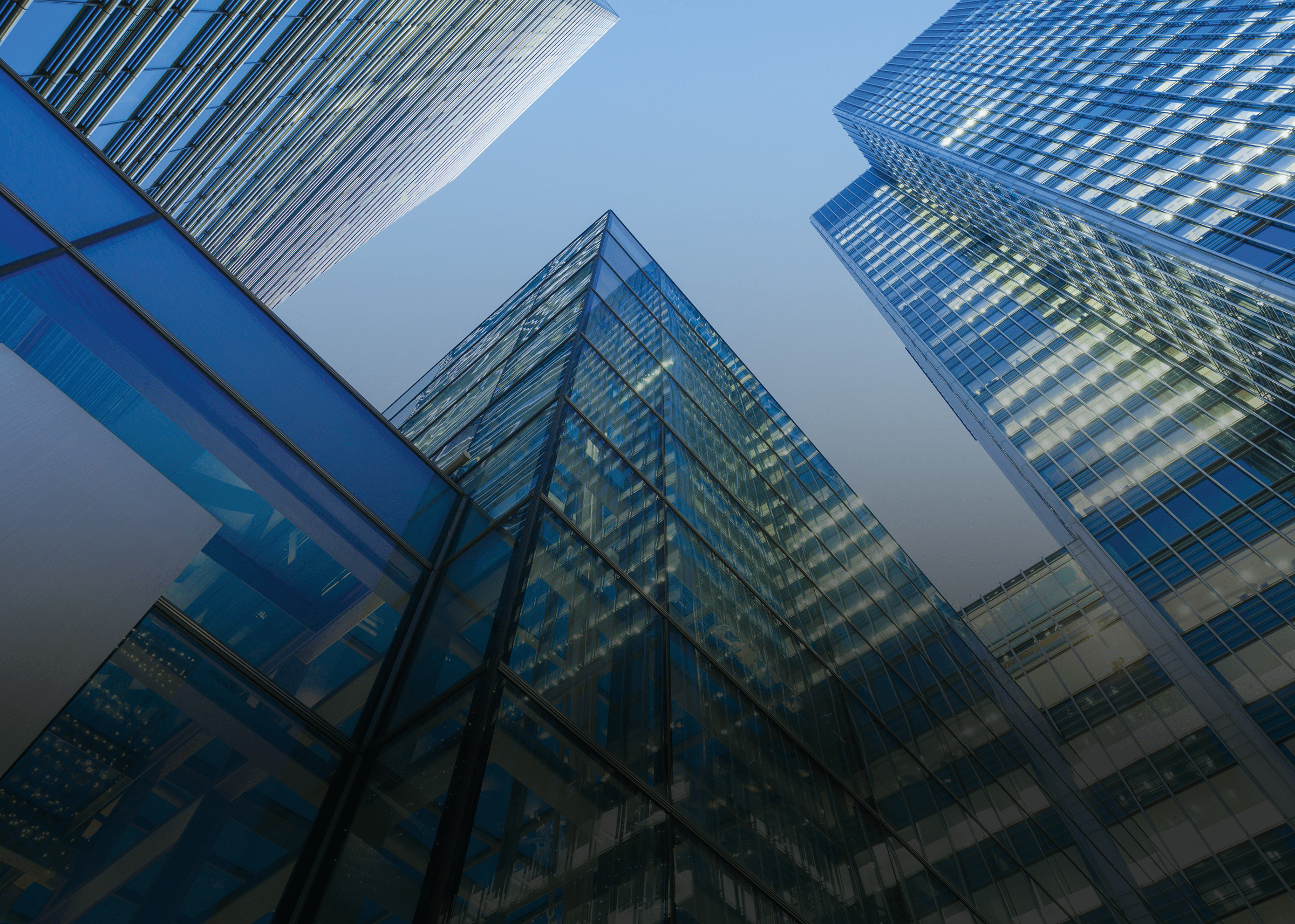 Looking up at modern glass skyscrapers with blue-tinted facades reflecting light against a clear sky.
