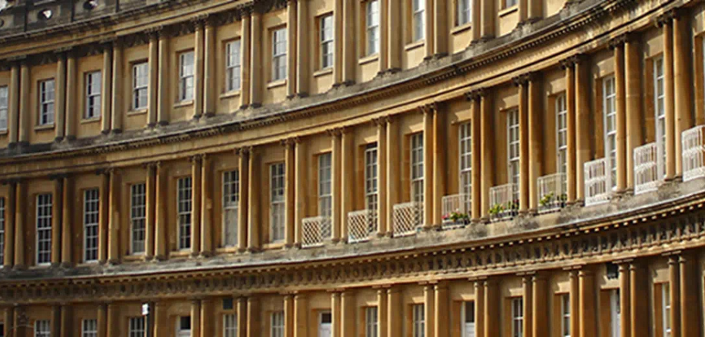 Close-up of the Royal Crescent in Bath, showing its curved Georgian architecture with honey-colored stone and white windows.