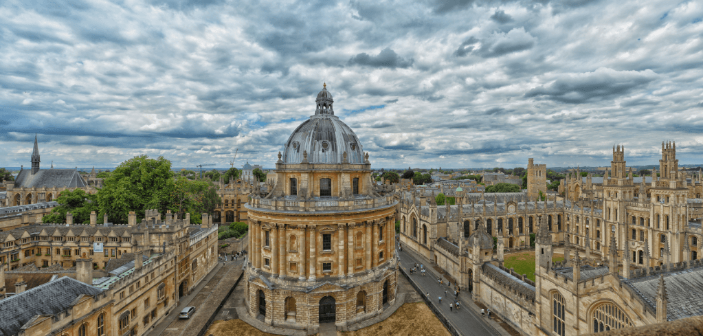 Aerial view of Oxford University with the Radcliffe Camera dome at center under dramatic cloudy skies.