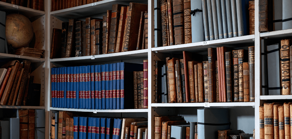 White bookshelves filled with antique leather-bound books in brown, blue, and red, with a vintage globe on the top shelf.