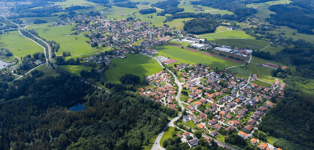 Aerial view of a rural European village with orange-roofed houses nestled among green fields and surrounding forests.