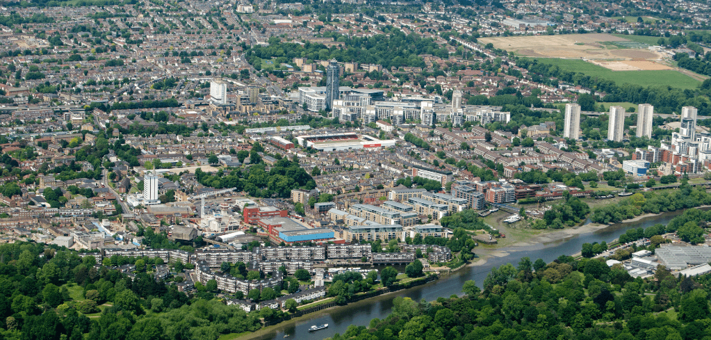 Aerial view of urban London neighborhood with residential buildings, high-rises, green spaces, and a river flowing through.