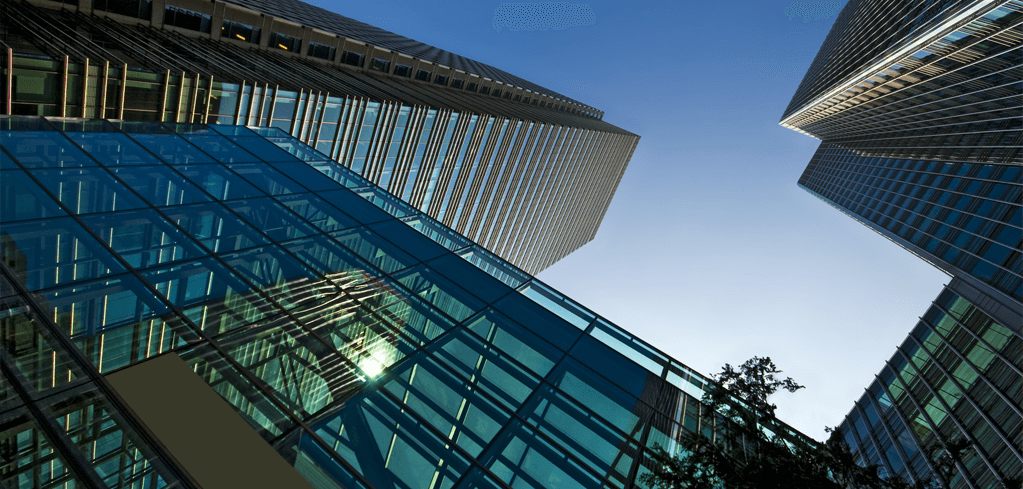 Looking up at modern glass skyscrapers with blue-tinted facades against a clear sky in an urban financial district.