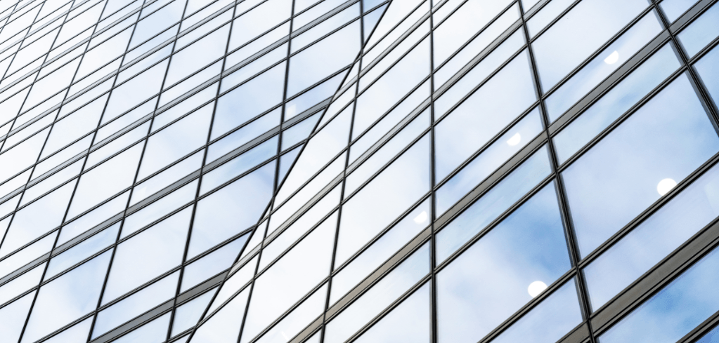 Carter Jonas LLP — Close-up of a modern glass office building facade reflecting a blue sky with clouds and sunlight glare.