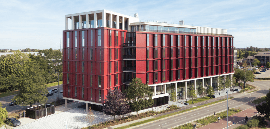 Aerial view of Merlin Place, a modern multi-story office building with a bold red facade, large windows, and a white rooftop structure.