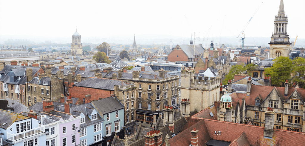 Aerial view of Oxford's historic cityscape with distinctive spires, stone buildings, and colorful rooftops on a misty day.