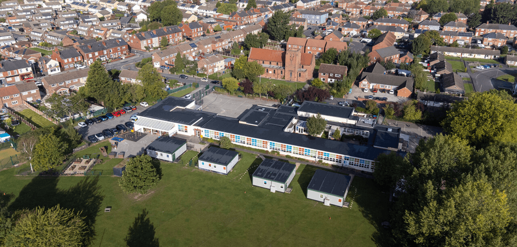 Aerial view of a school campus with colorful windows, surrounded by residential neighborhoods and a brick church nearby.