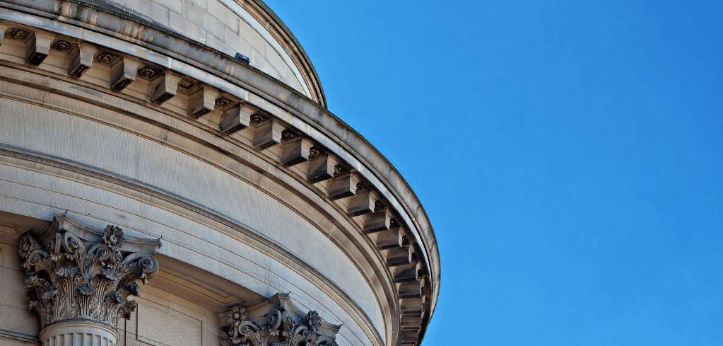 Close-up of a neoclassical stone dome with ornate Corinthian columns against a clear blue sky.
